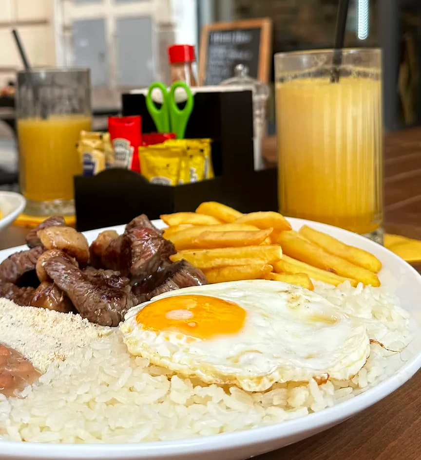 Il piatto del pranzo al tavolo fuori: riso, fagioli, farofa, carne con l'aglio, patatine e uovo