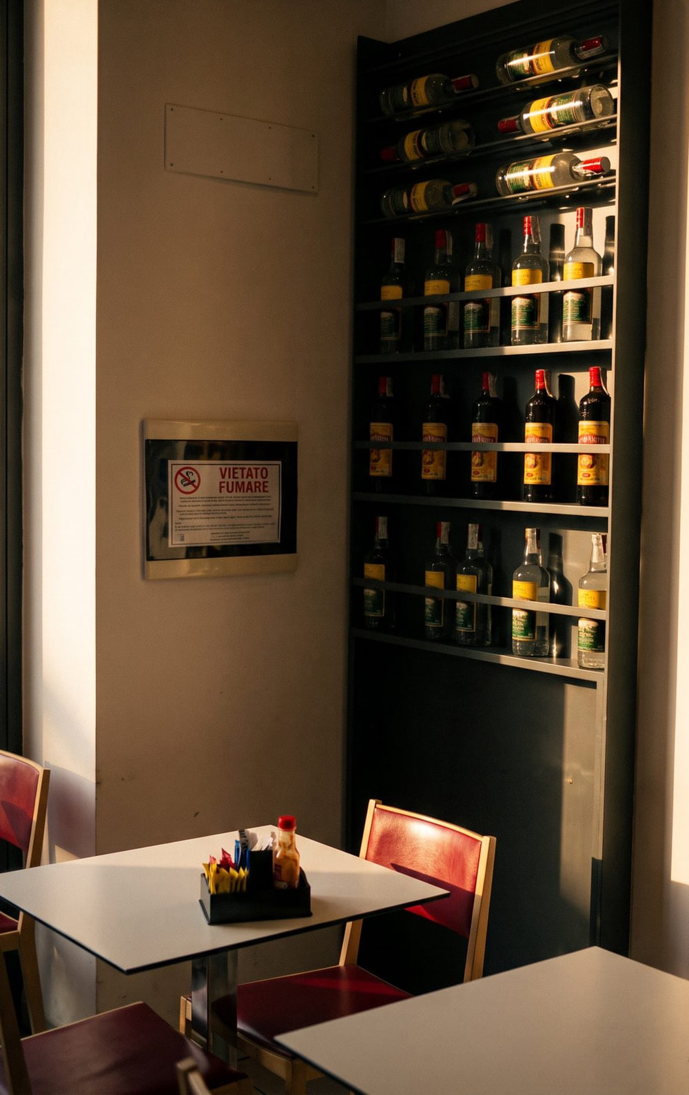 La sala: la nicchia degli scaffali con le bottiglie di cachaça, i tavoli bianchi e le sedie bordeaux